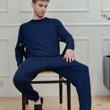 Man in navy blue loungewear set and black slippers sitting on a chair in modern room
