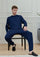 Man in navy blue loungewear set and black slippers sitting on a chair in modern room