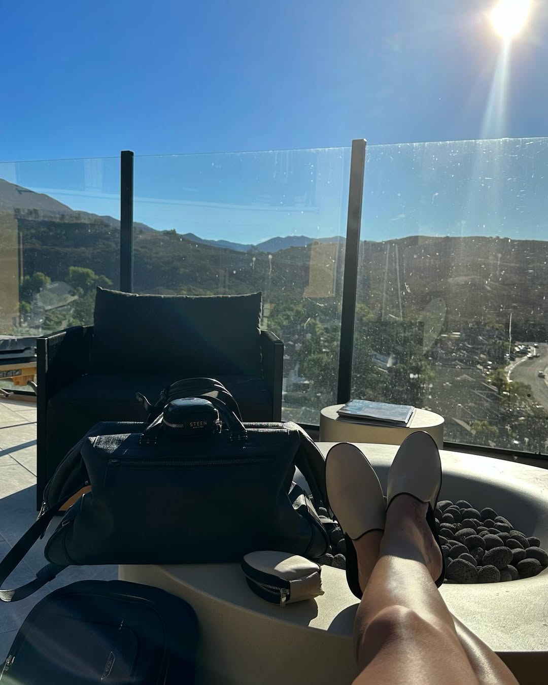 Relaxing legs by rooftop fire pit, luxury travel bag, scenic mountain view, sunny day