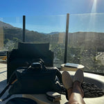 Relaxing legs by rooftop fire pit, luxury travel bag, scenic mountain view, sunny day
