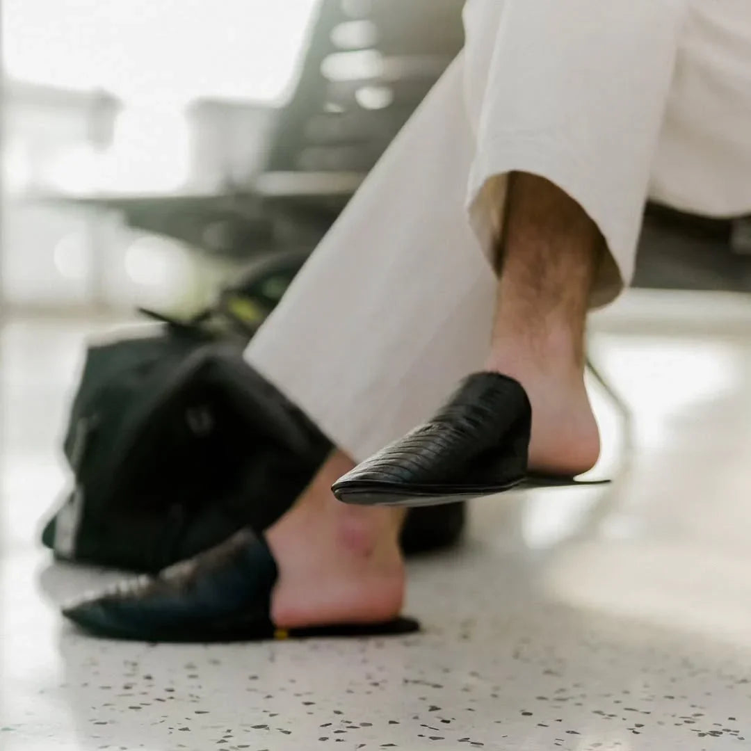 Man in white pants wearing black leather slippers at airport waiting area