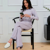 Woman in light gray pajamas and white slippers sitting on chair using smartphone indoors
