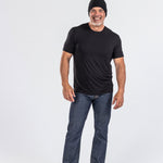 Smiling man wearing a black cashmere hat, black t-shirt, jeans, and loafers, studio backdrop