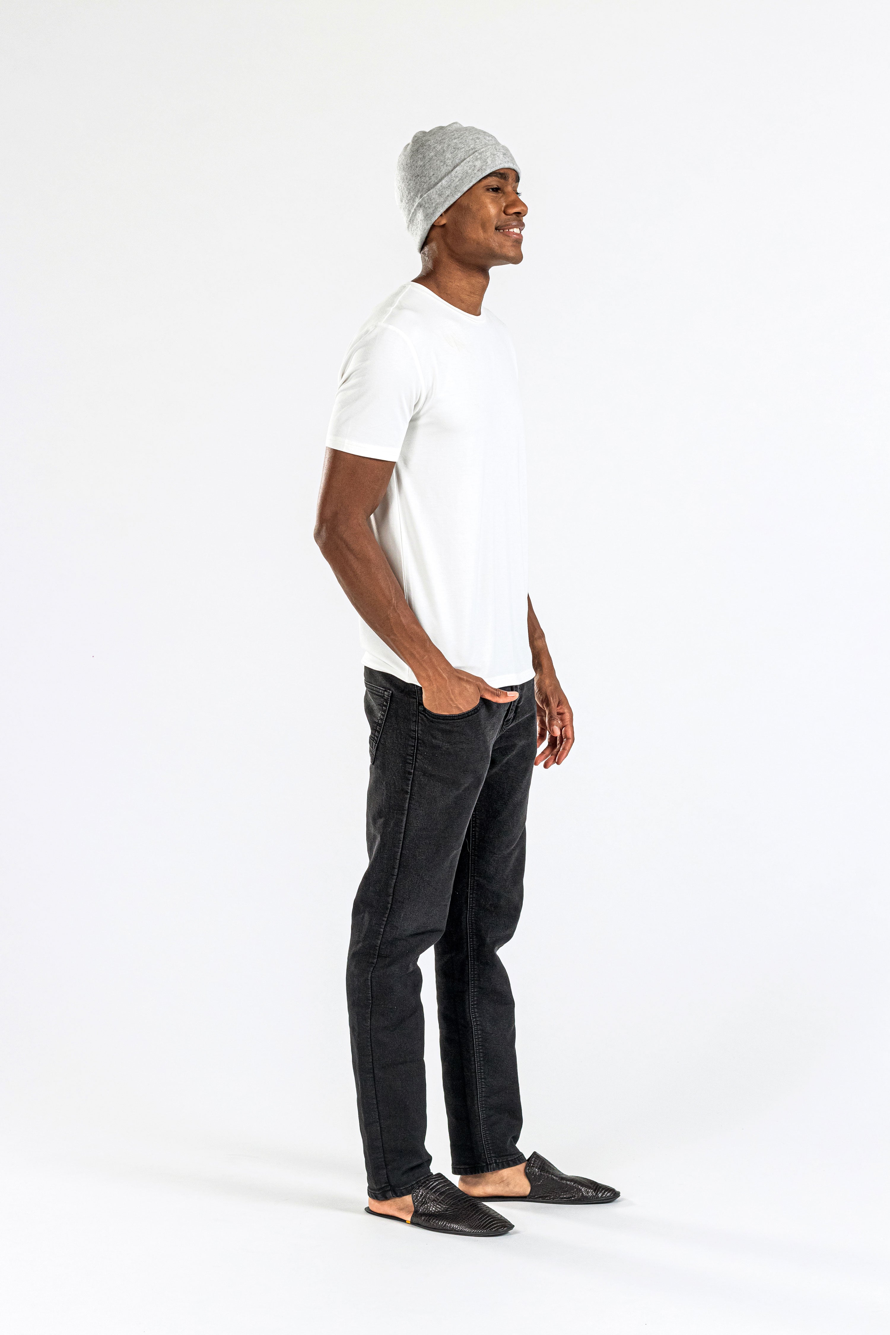 Man wearing grey cashmere hat, white t-shirt, black jeans, loafers on white background