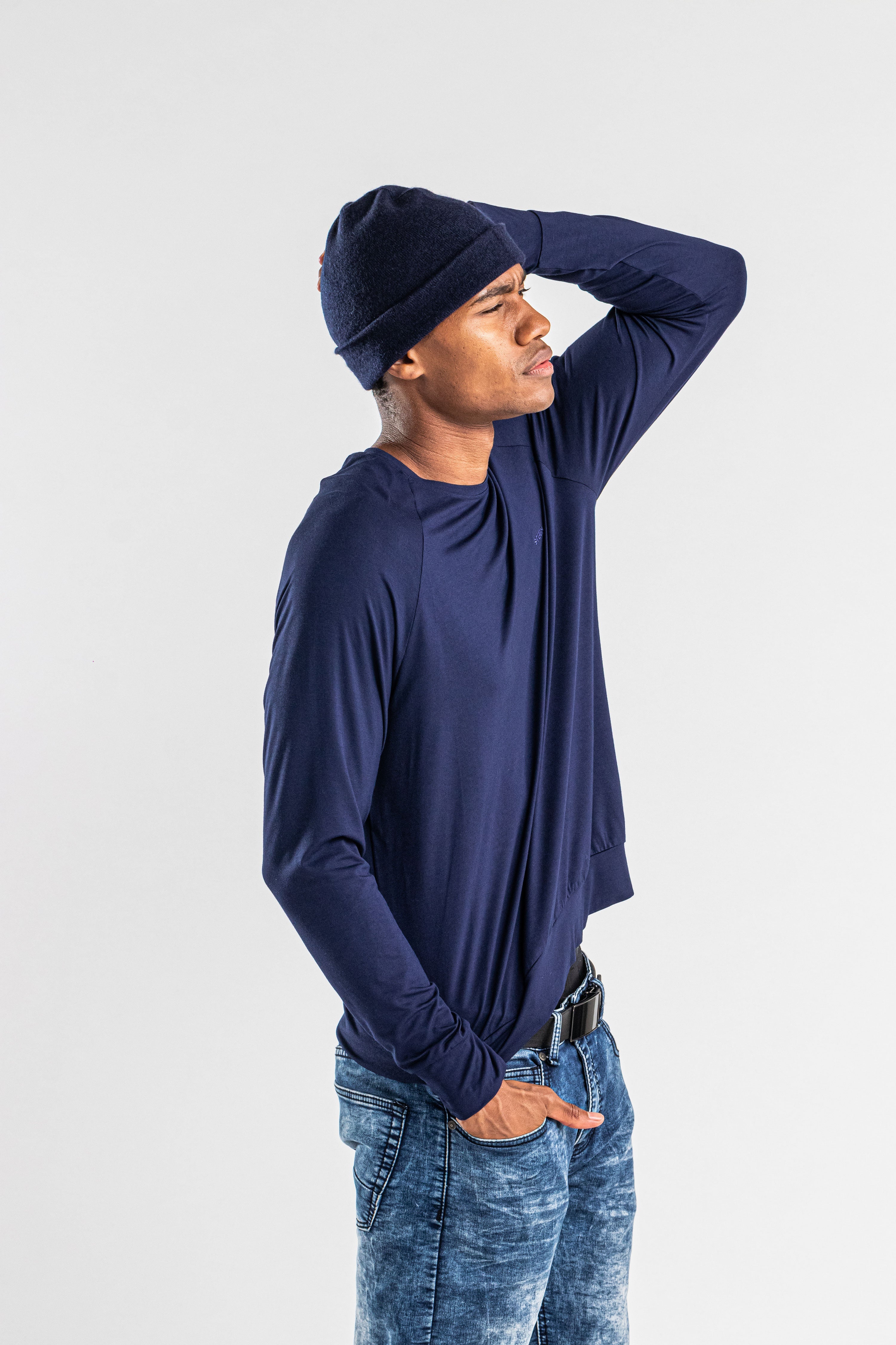 Man wearing navy cashmere hat and long sleeve shirt with jeans on white background