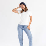 Woman wearing navy cashmere hat, white t-shirt, blue jeans, and black shoes on white backdrop