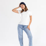 Woman wearing navy cashmere hat, white t-shirt, blue jeans, and black shoes on white backdrop