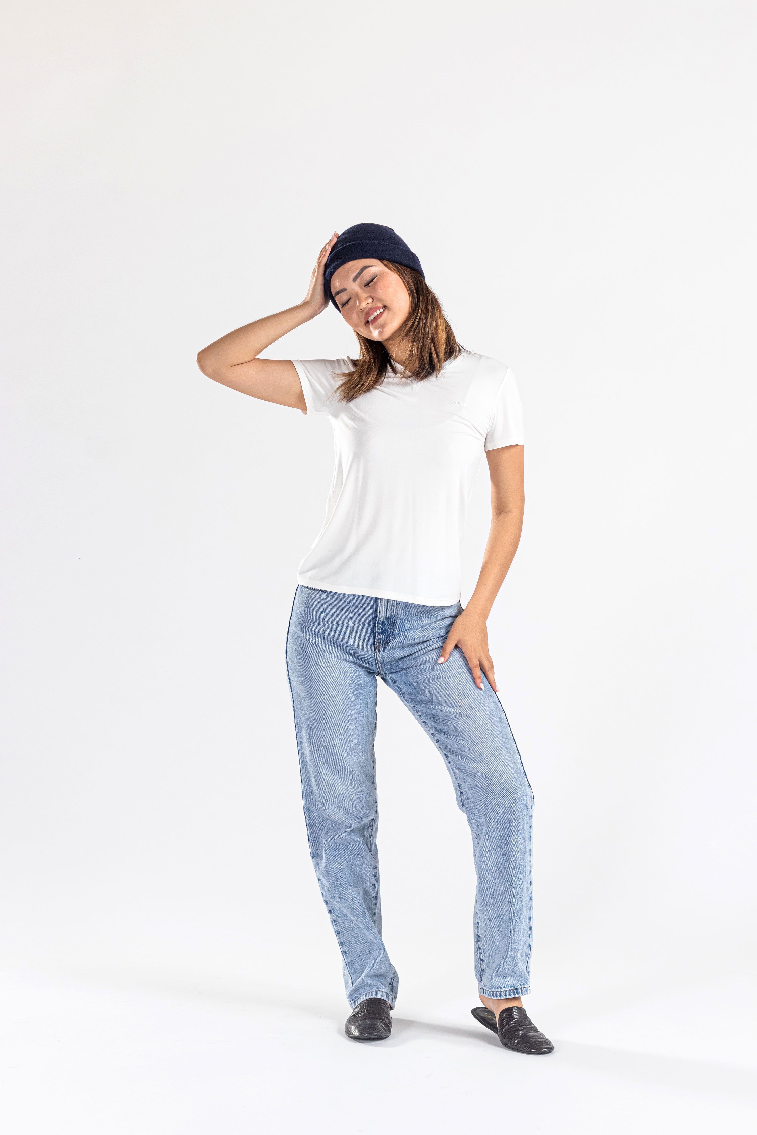 Woman wearing navy cashmere hat, white t-shirt, blue jeans, and black shoes on white backdrop