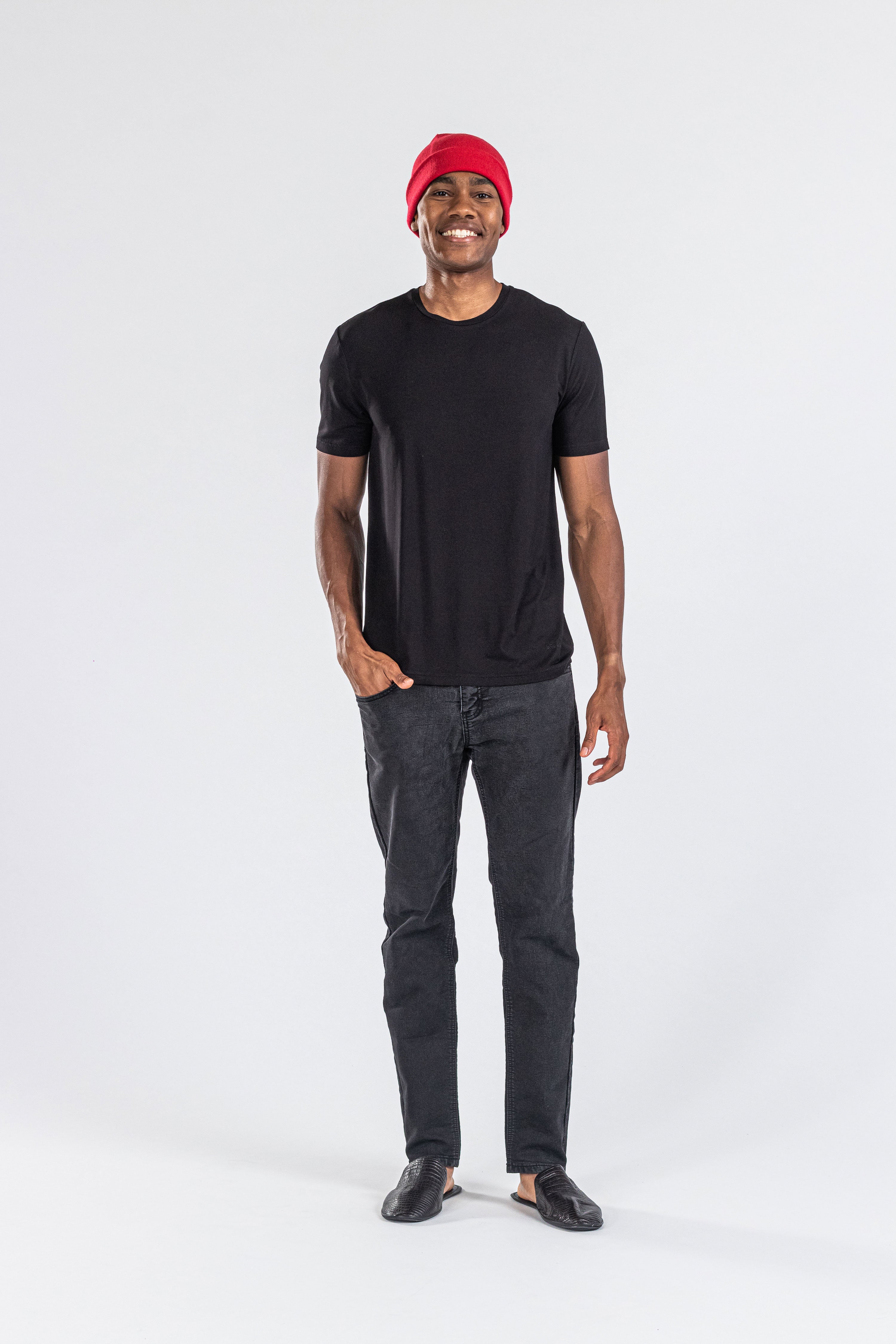 Man wearing a red cashmere hat, black t-shirt, and black pants against white background