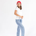 Woman wearing red cashmere hat, white t-shirt, and light blue jeans on white background