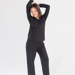 Woman in black long sleeve loungewear set posing barefoot on white background