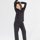 Woman in black long sleeve loungewear set posing barefoot on white background