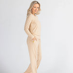 Woman in cream loungewear set poses barefoot against a plain white background