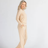 Woman in cream loungewear set poses barefoot against a plain white background