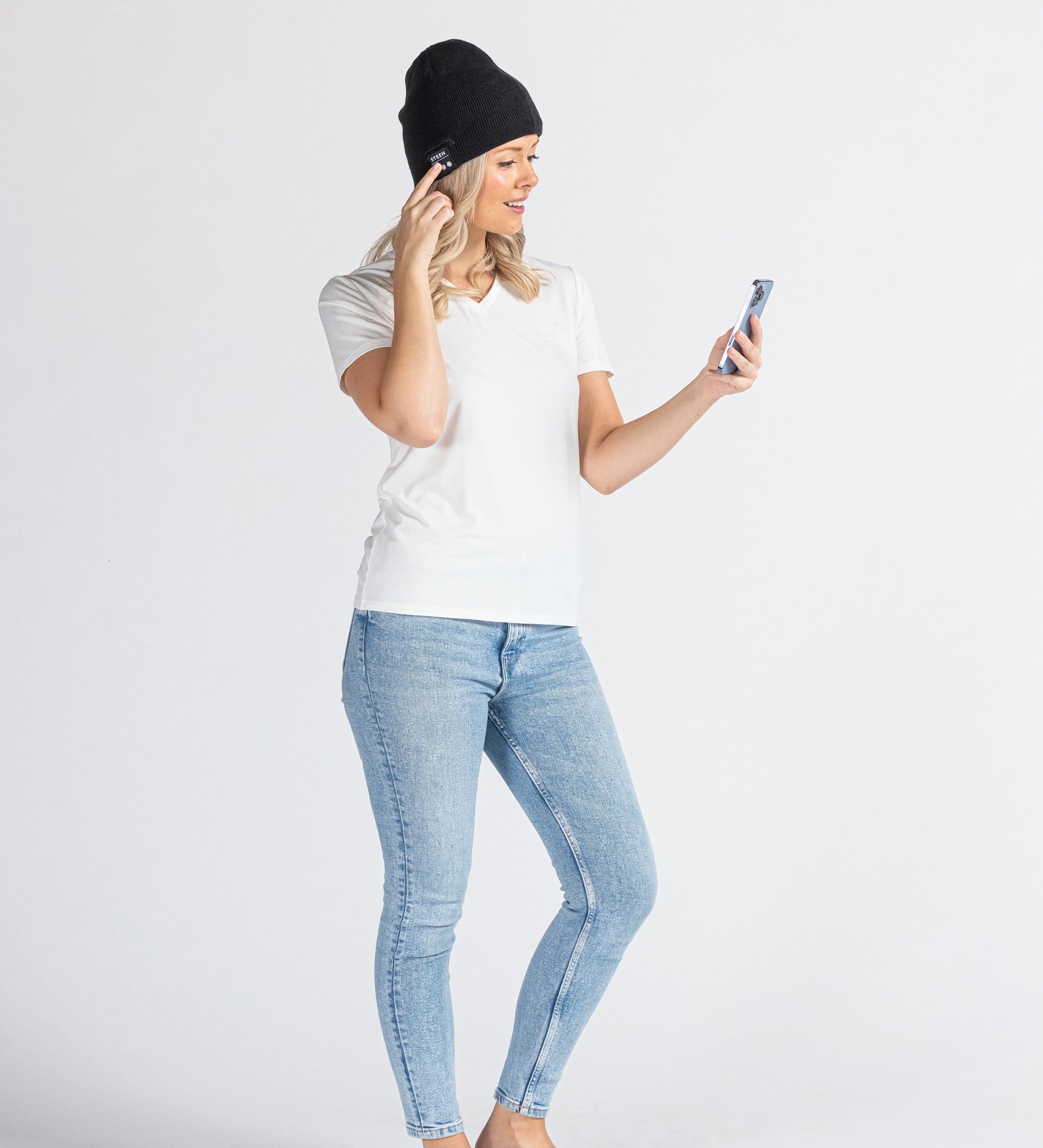 Woman wearing a black music beanie and jeans using smartphone on white background