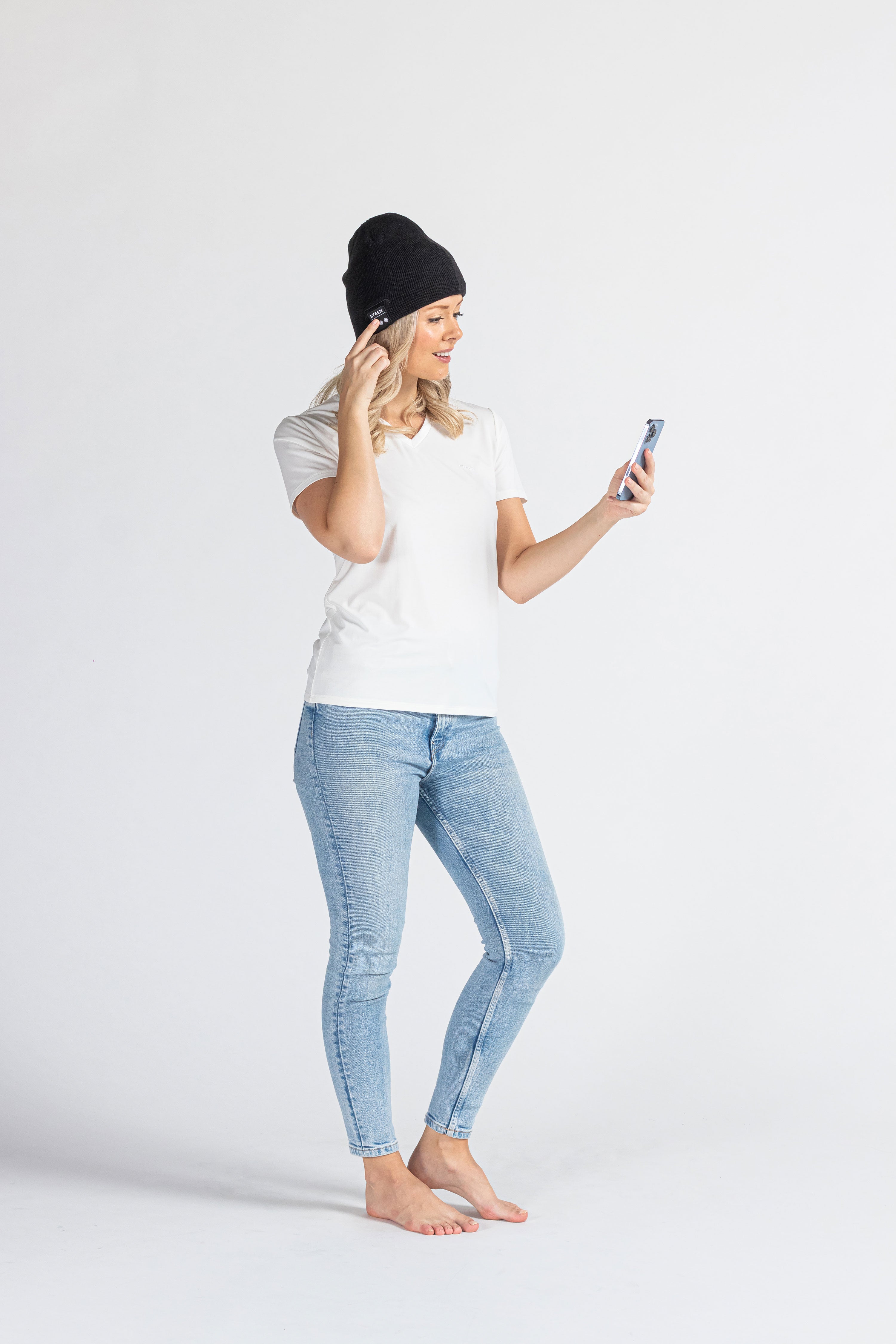 Woman wearing a black music beanie and jeans using smartphone on white background