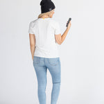 Woman wearing black music beanie, white t-shirt, jeans, holding phone, studio background