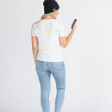 Woman wearing black music beanie, white t-shirt, jeans, holding phone, studio background