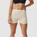 Woman wearing beige seamless shorts and a black lace bra on a plain background
