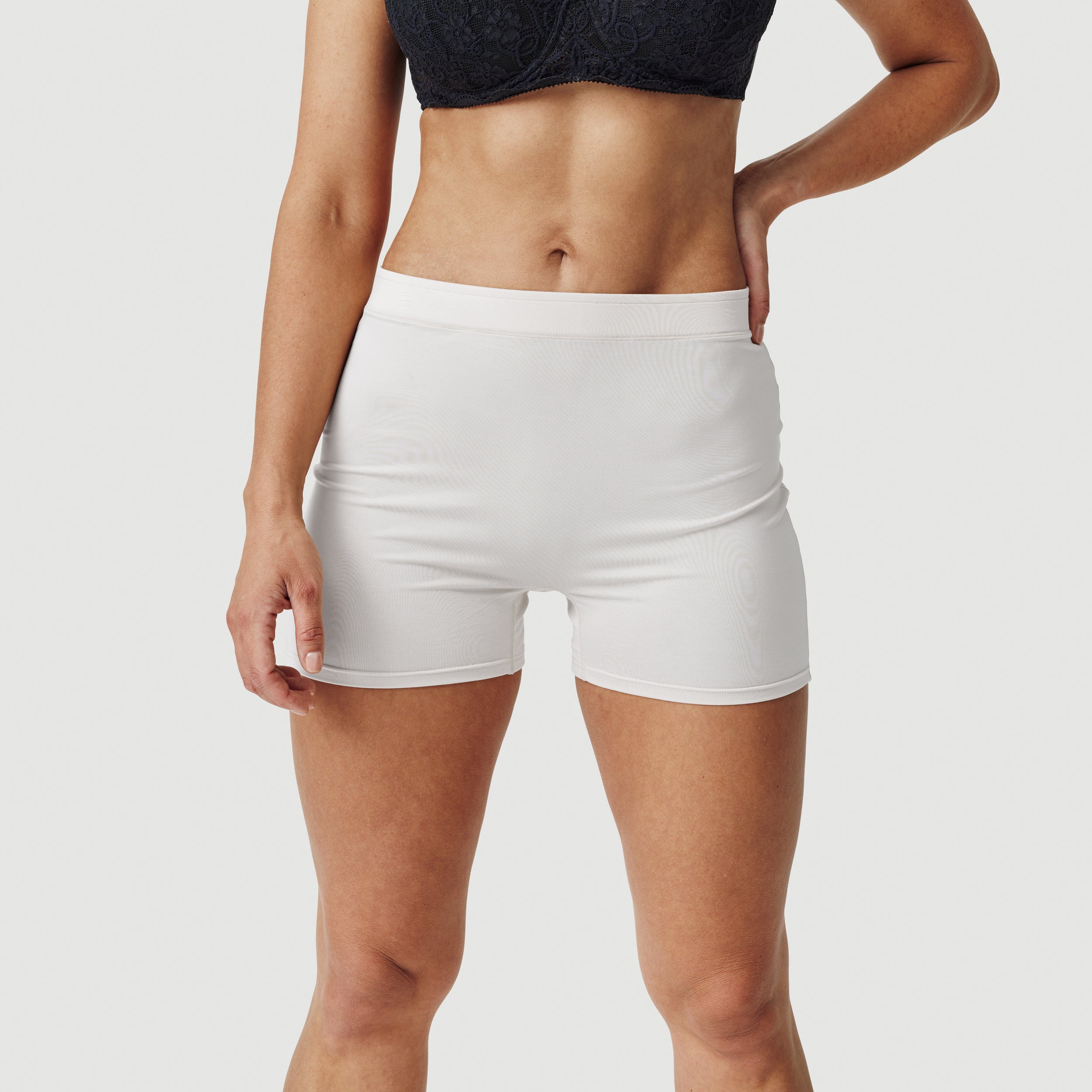 Woman wearing white seamless boxer shorts and a black lace bralette on white background