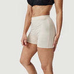 Woman wearing beige high-waisted boxer briefs and black lace bralette on white background