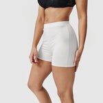 Woman wearing white high-waist shorts and black lace bra against plain background