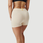 Woman wearing beige boxer briefs and a black bra on a plain white background