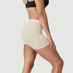 Woman in beige seamless shorts and black bra posing against white background