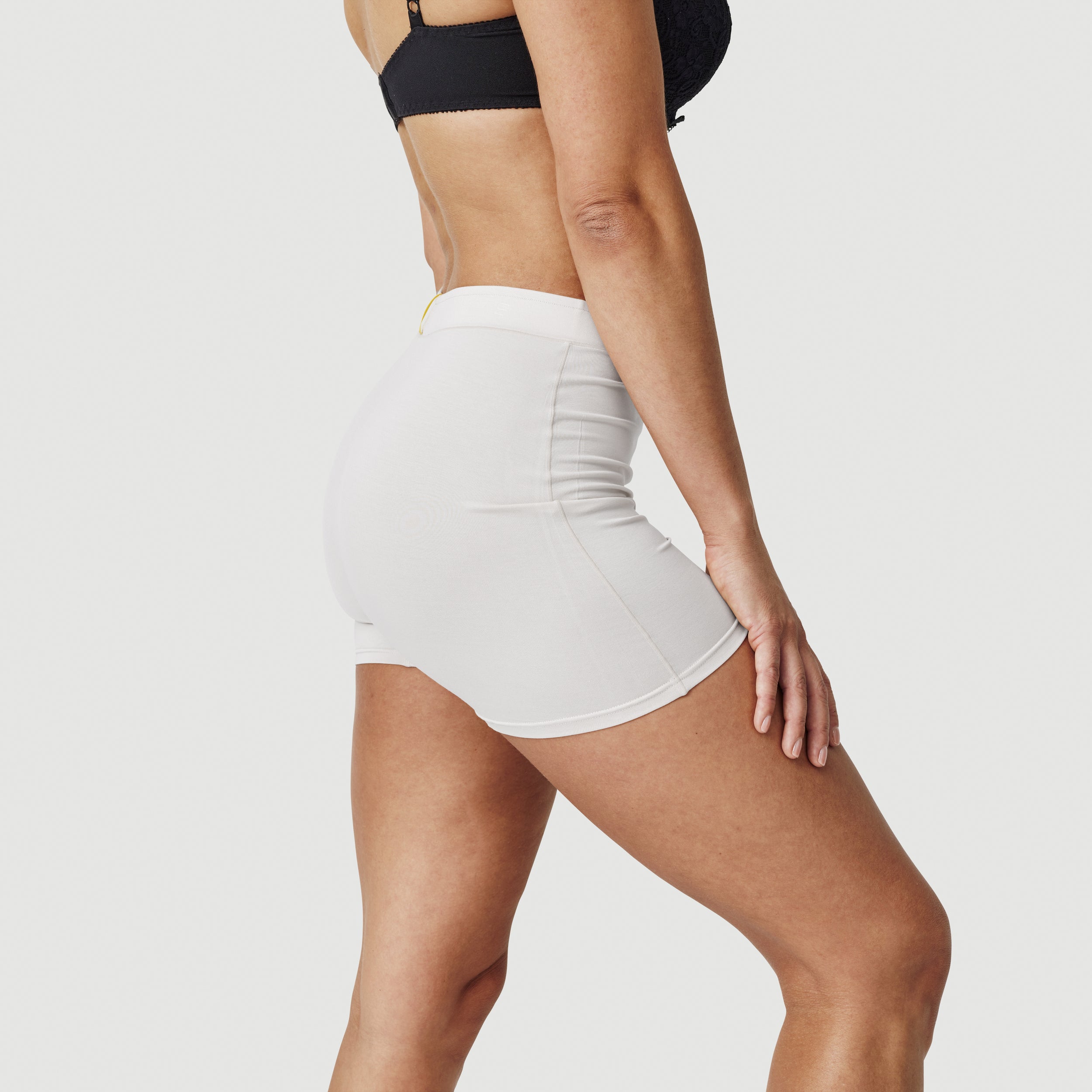 Woman in black bra and white high-waisted shorts posing against white background
