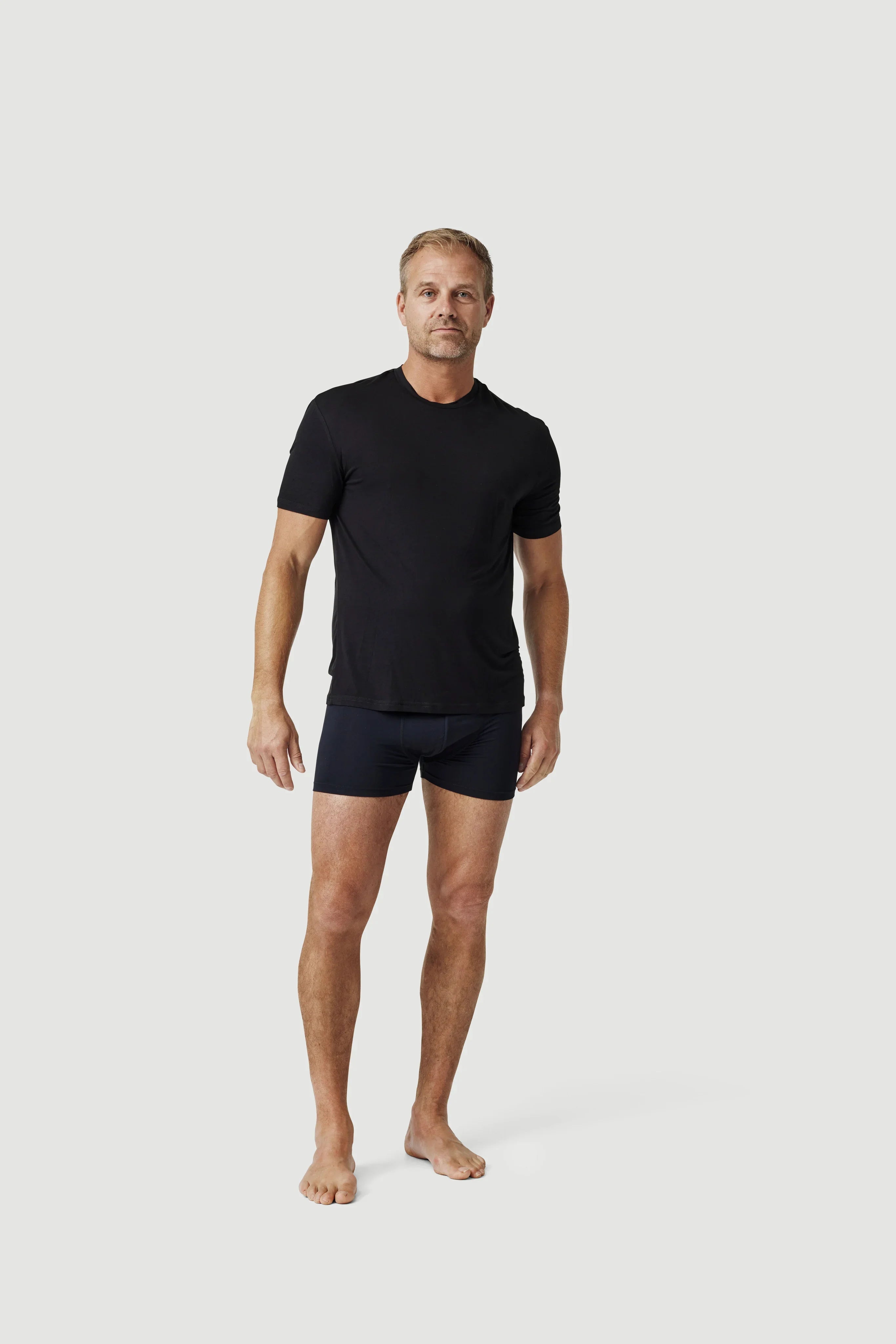 Man wearing black t-shirt and boxer briefs on plain light background