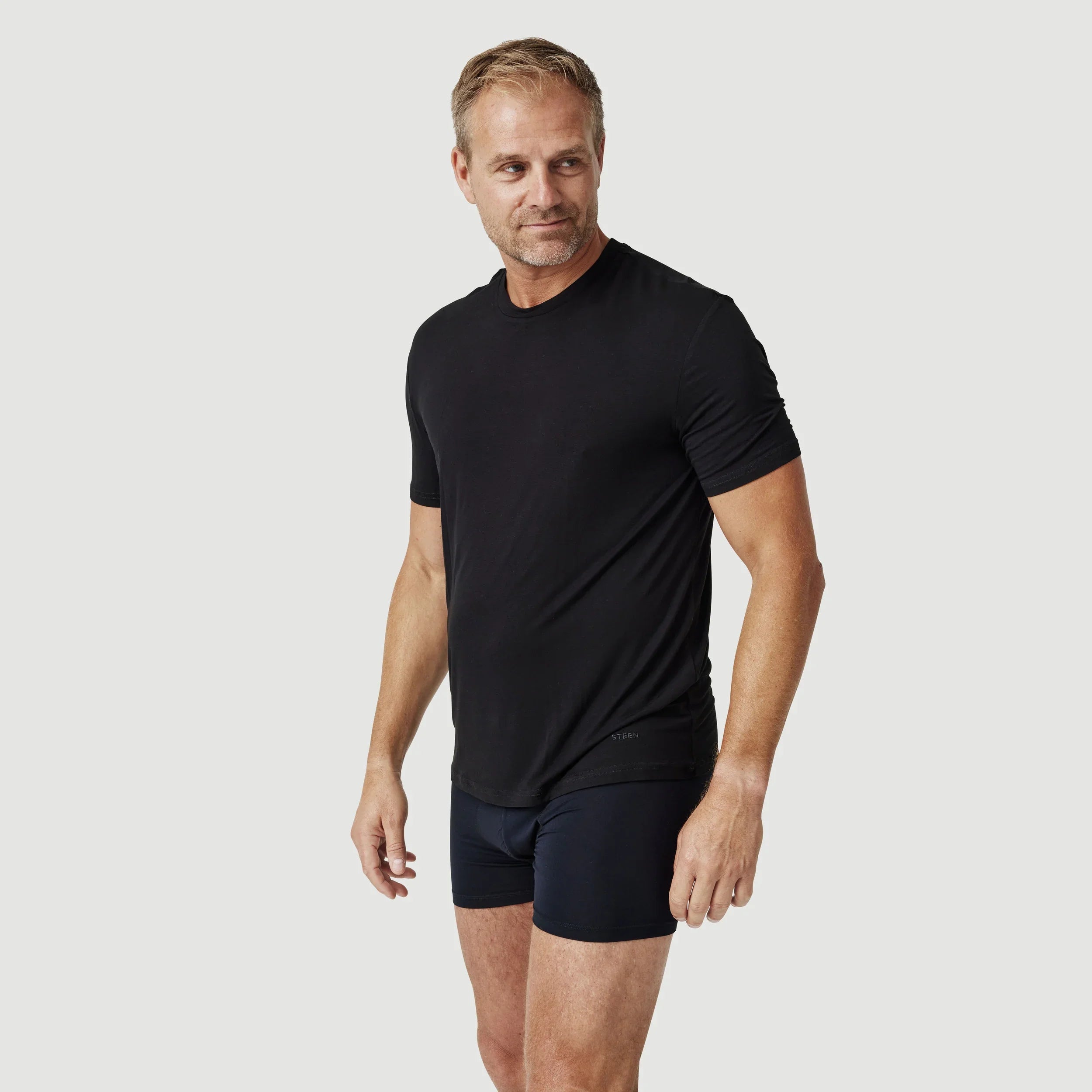 Man wearing black t-shirt and black boxer briefs on a plain light background