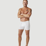 Smiling man with tattoos modeling white boxer briefs on plain background
