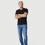 Man in black t-shirt and blue jeans standing barefoot against white background