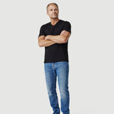 Man in black t-shirt and blue jeans standing barefoot against white background