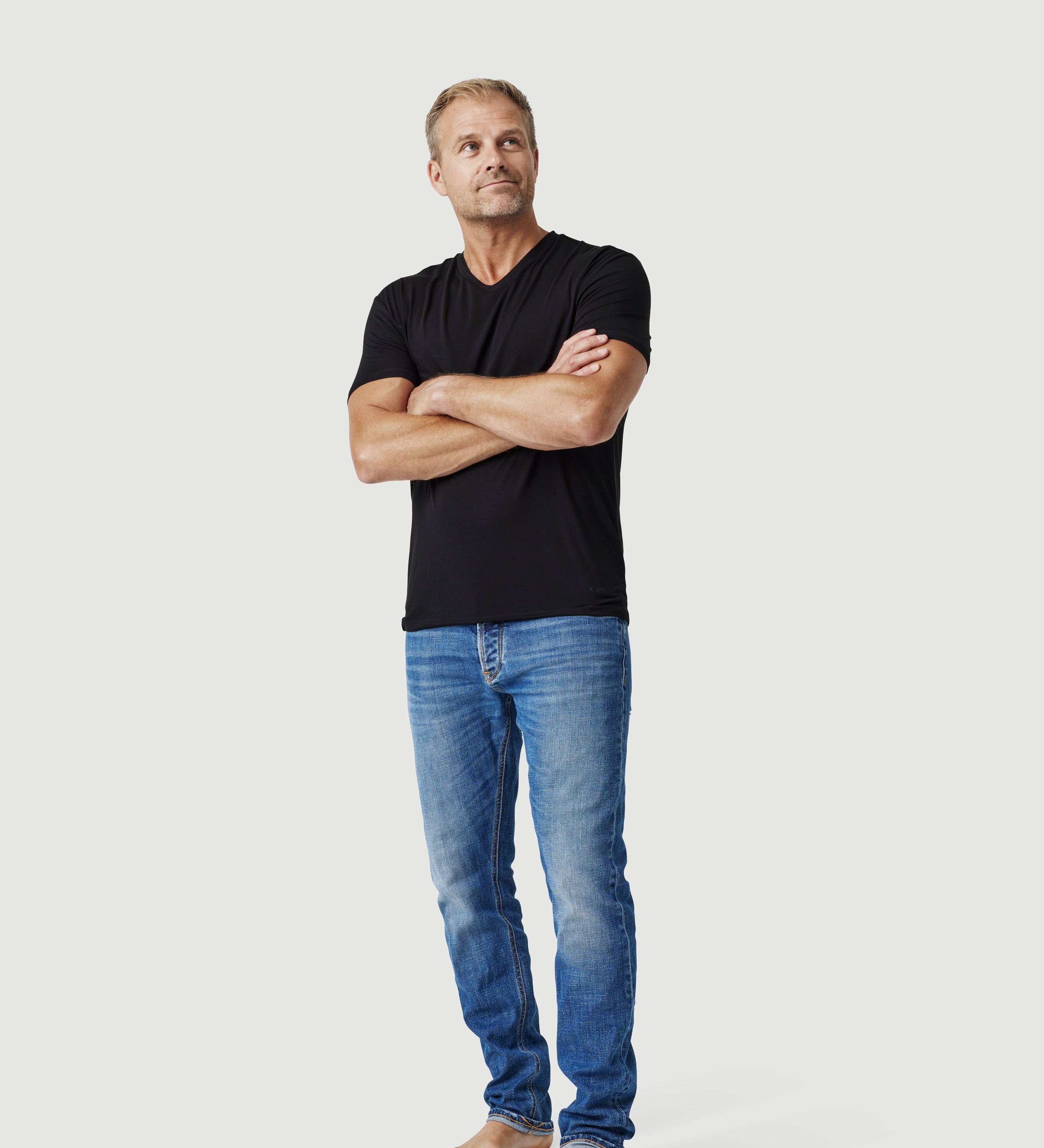 Man in black t-shirt and blue jeans standing barefoot against white background