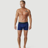 Man modeling blue boxer briefs against plain white background for men's underwear lookbook