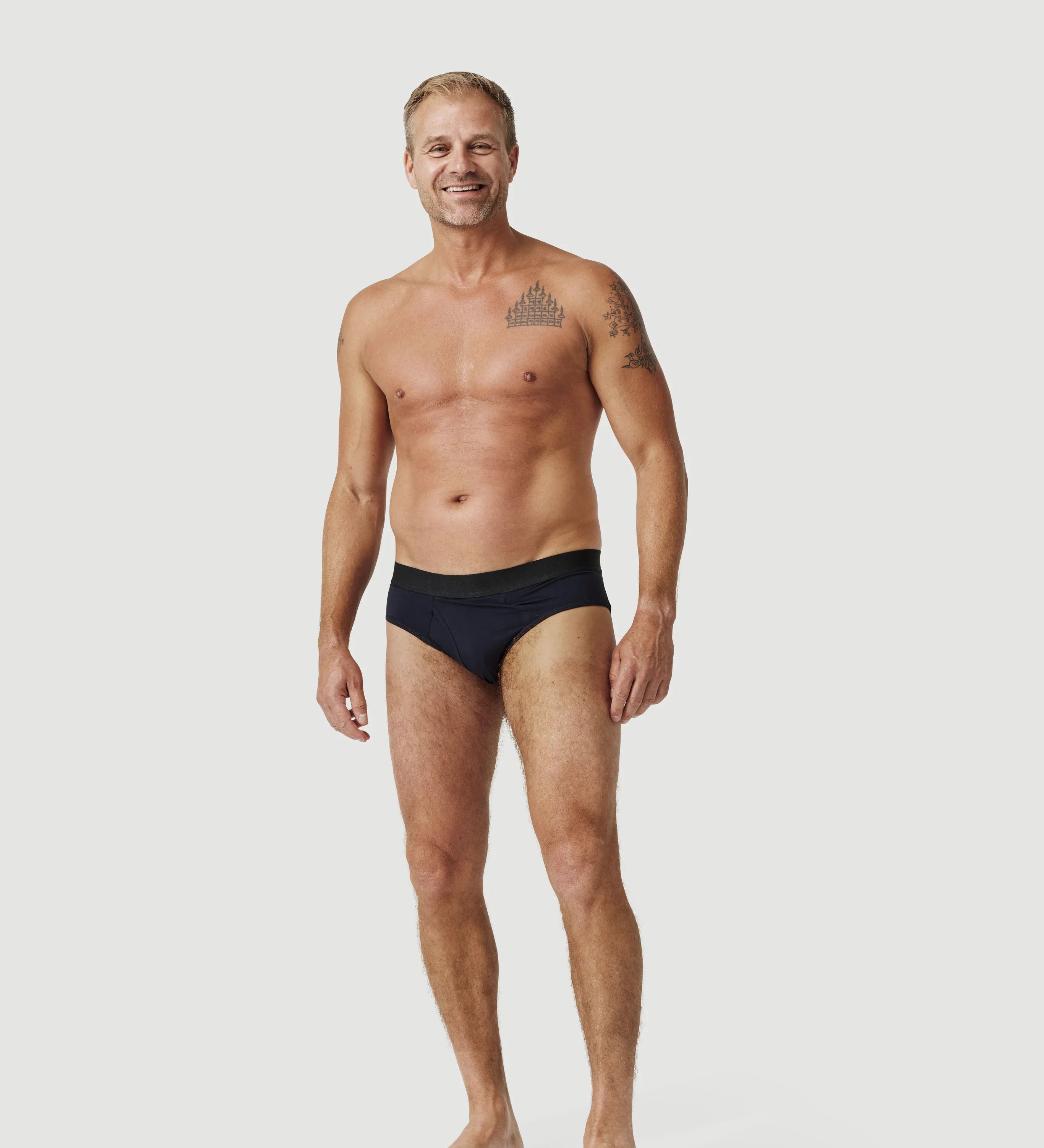 Smiling man wearing black men's swim briefs against a plain white background