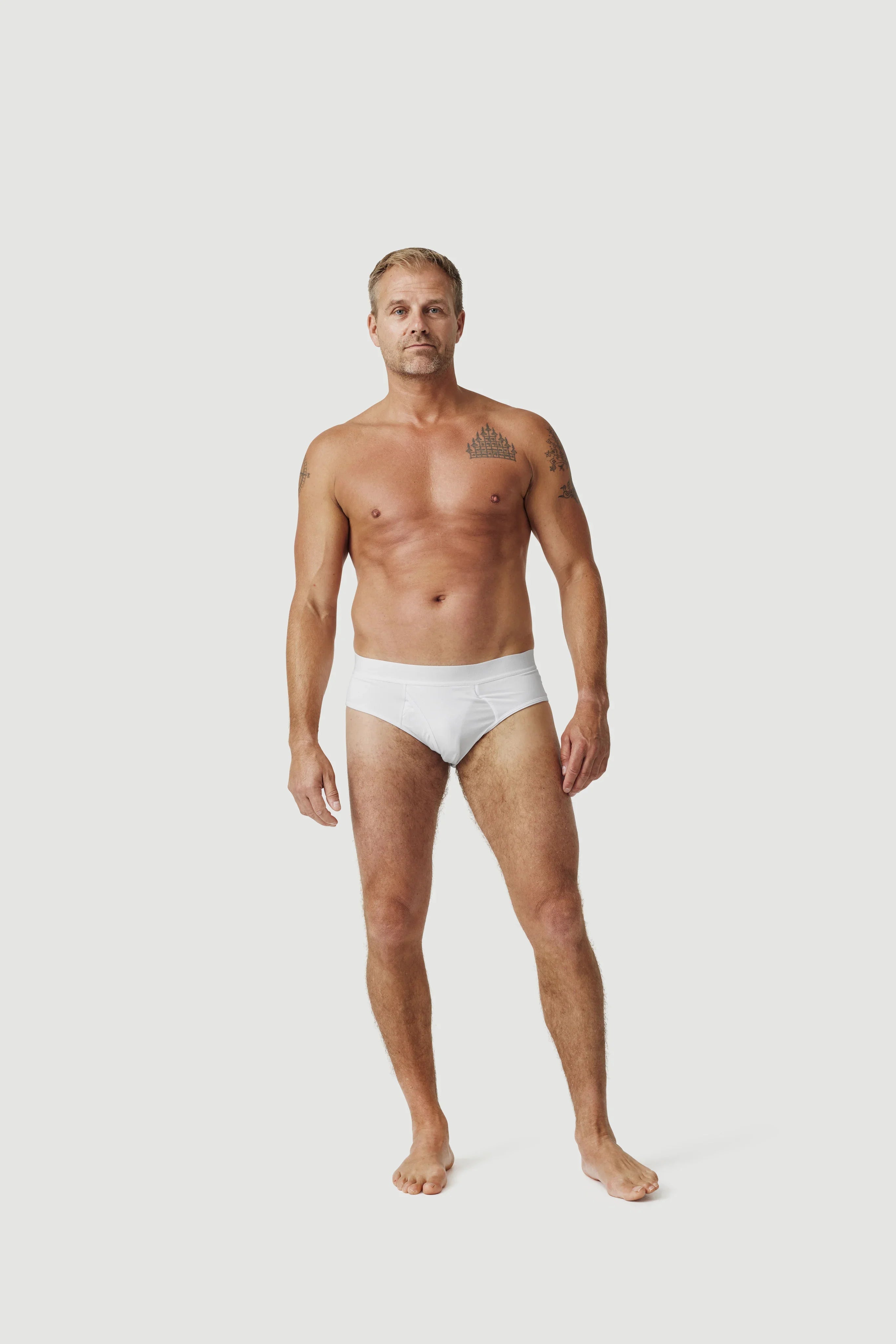 Tattooed man modeling white briefs underwear on plain white background