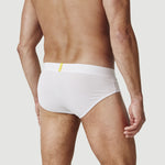 Man wearing white briefs underwear with yellow tag, shown from the back against plain background