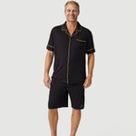 Man wearing black short-sleeve pajama set with yellow trim on plain background