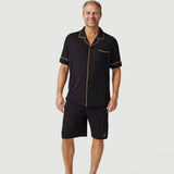 Man wearing black short-sleeve pajama set with yellow trim on plain background