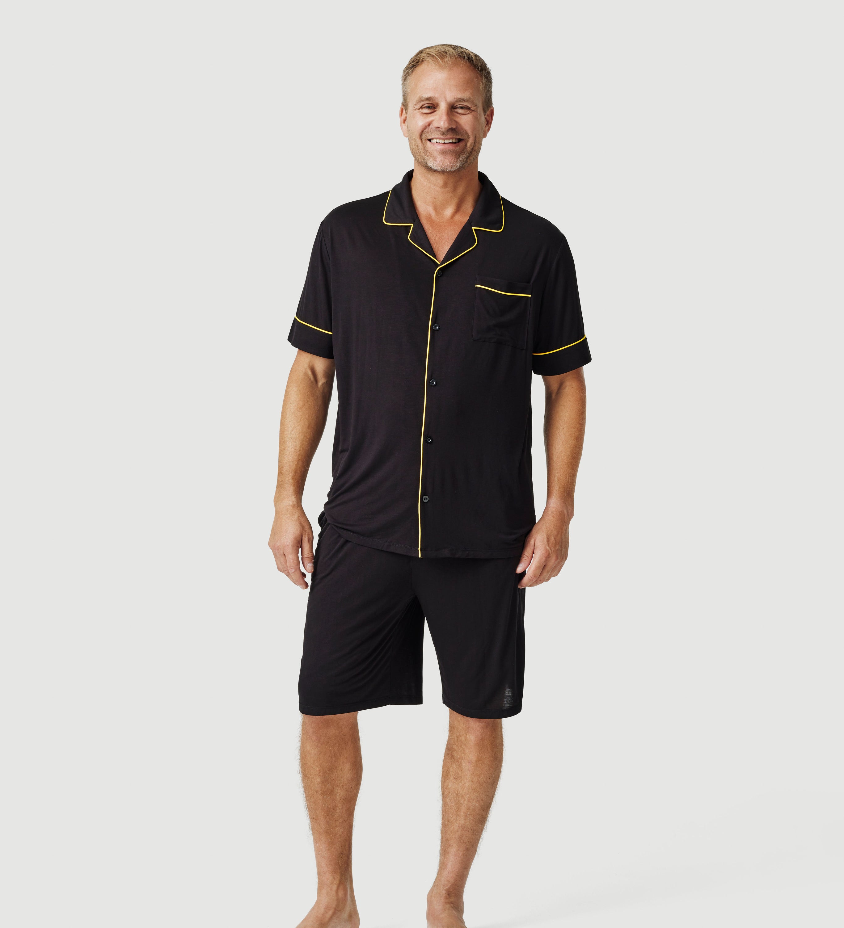 Man wearing black short-sleeve pajama set with yellow trim on plain background