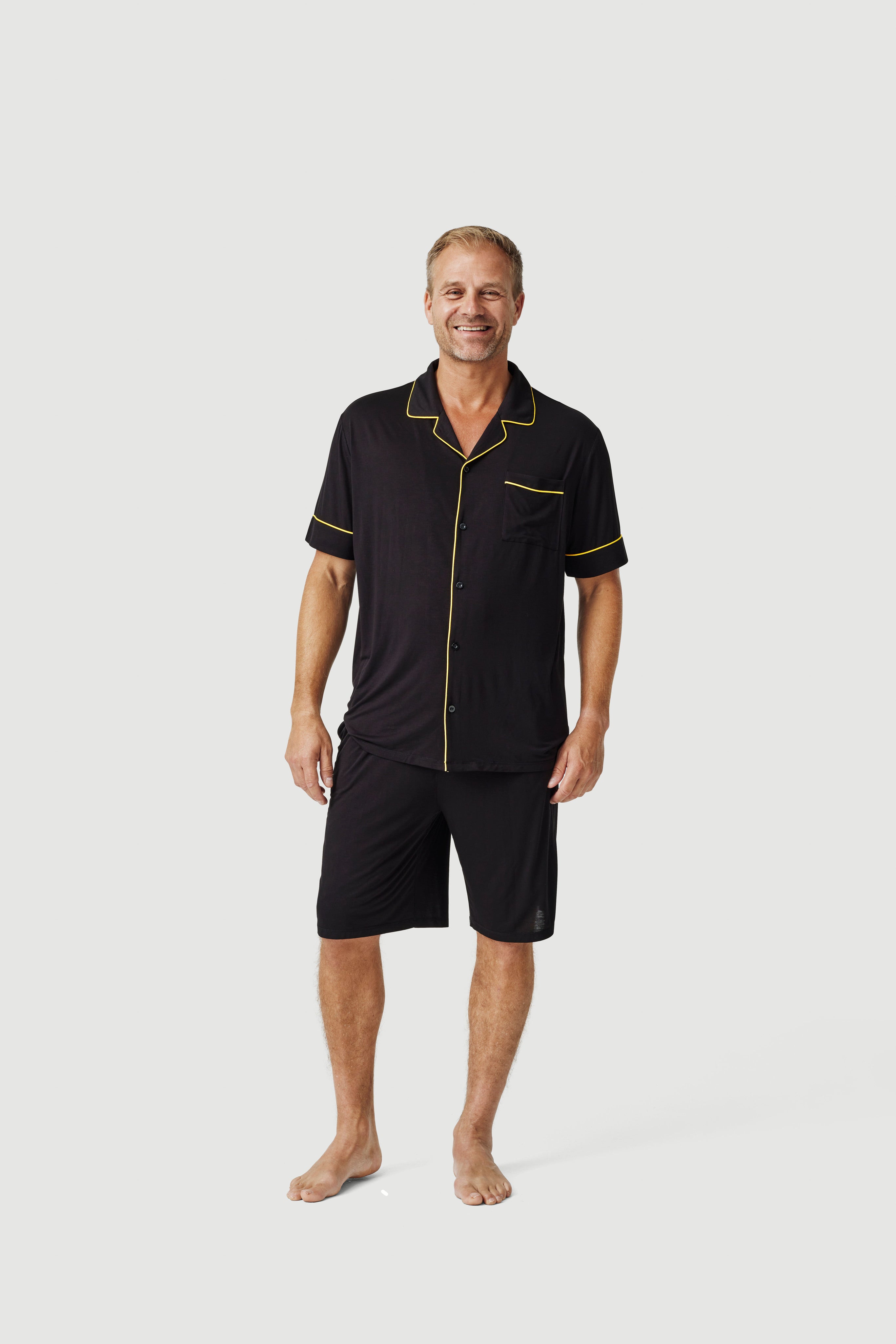 Man wearing black short-sleeve pajama set with yellow trim on plain background