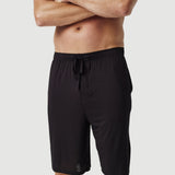 Man wearing black drawstring lounge shorts on white background, tattoos visible