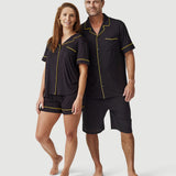 Man and woman wearing matching black short sleeve pajamas with yellow piping, on white background