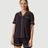 Woman wearing black short sleeve pajamas with yellow piping trim on plain background