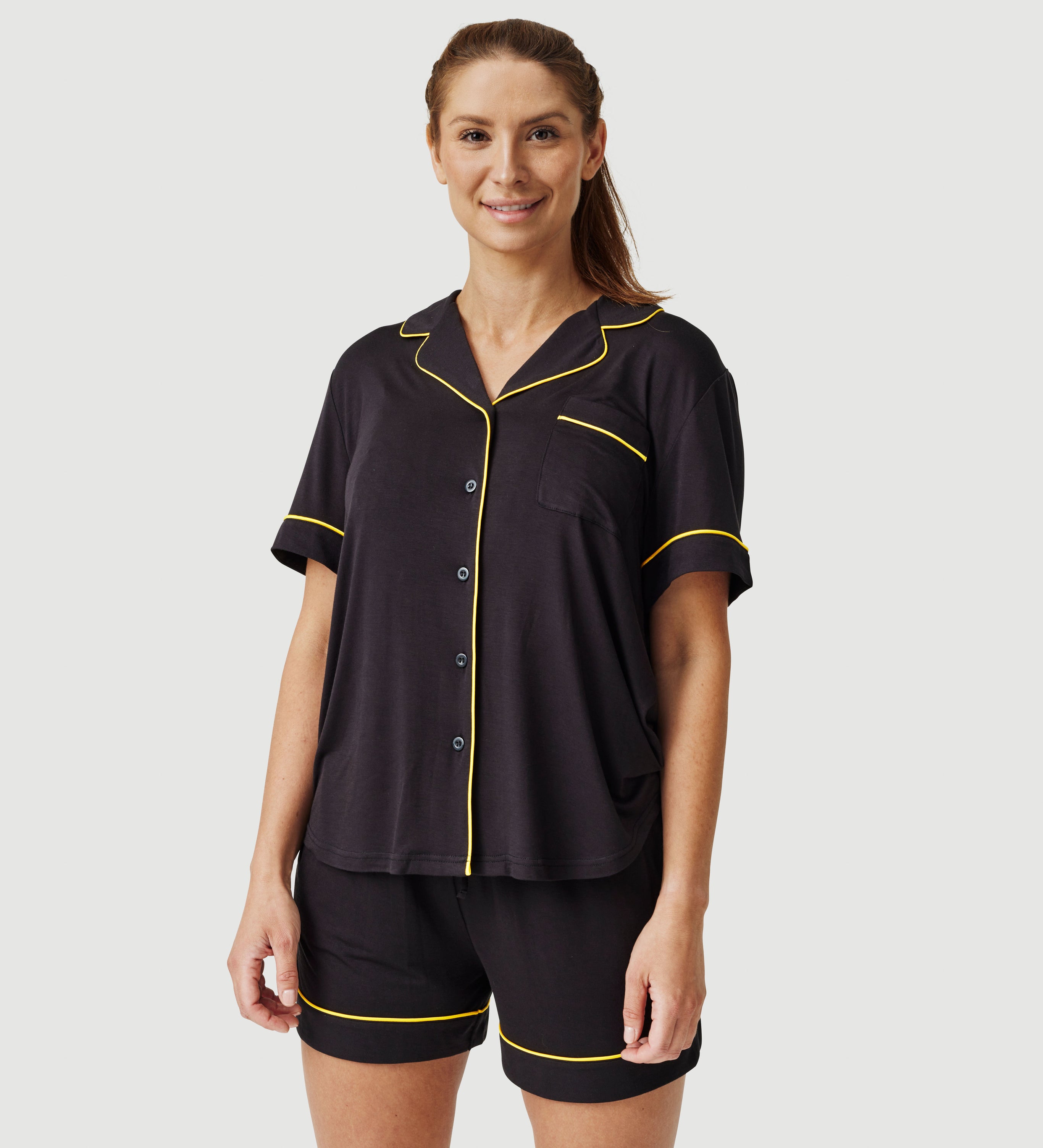 Woman wearing black short sleeve pajamas with yellow piping trim on plain background