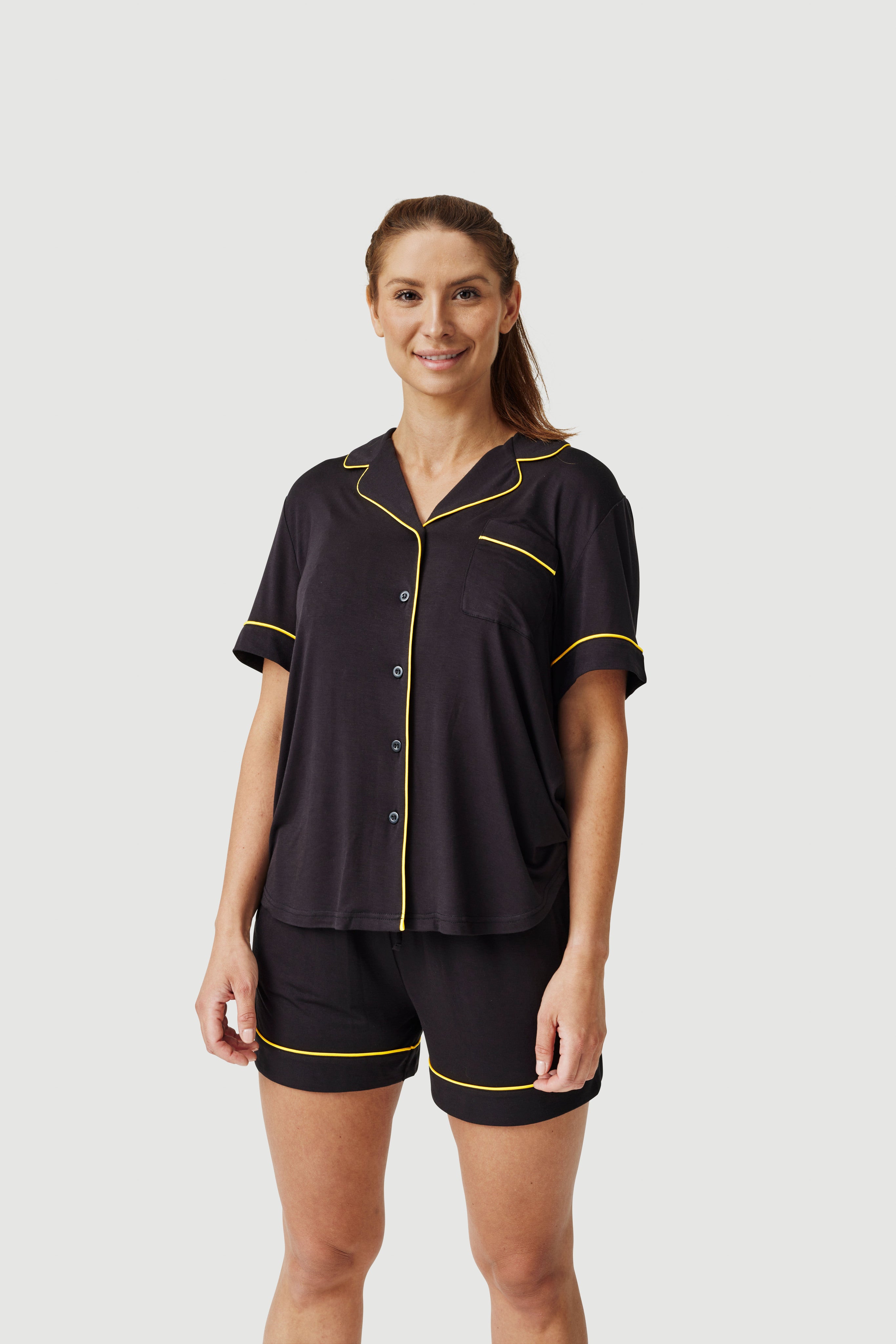 Woman wearing black short sleeve pajamas with yellow piping trim on plain background