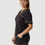 Woman wearing black pajama shorts set with yellow piping, posing against white background