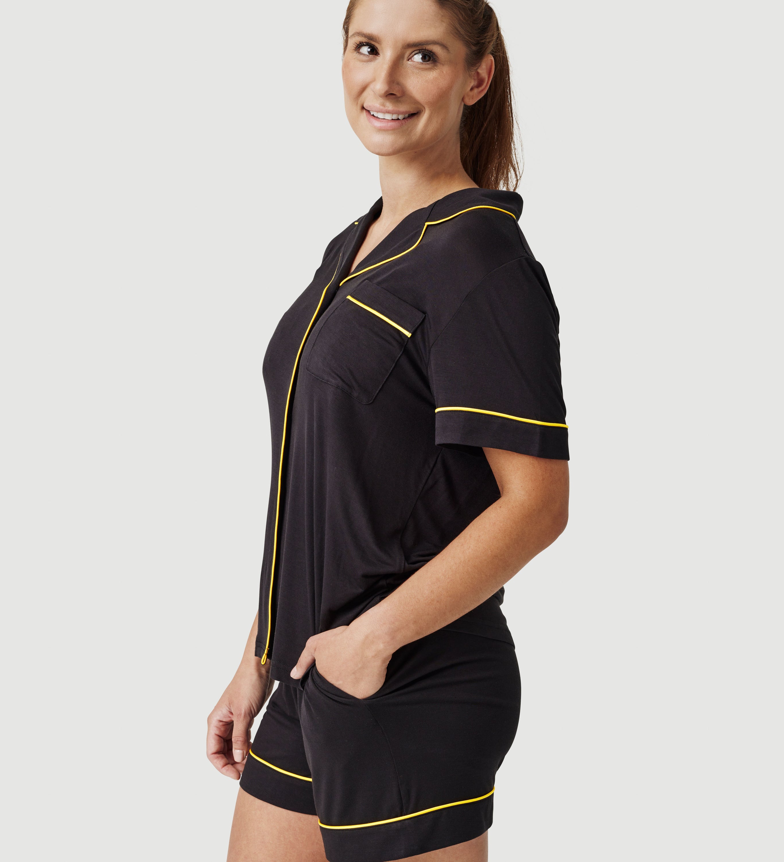 Woman wearing black pajama shorts set with yellow piping, posing against white background